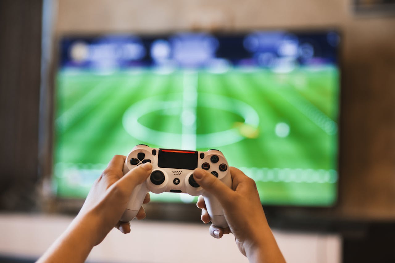 Home Close-up of hands holding a game controller playing a football video game on screen.