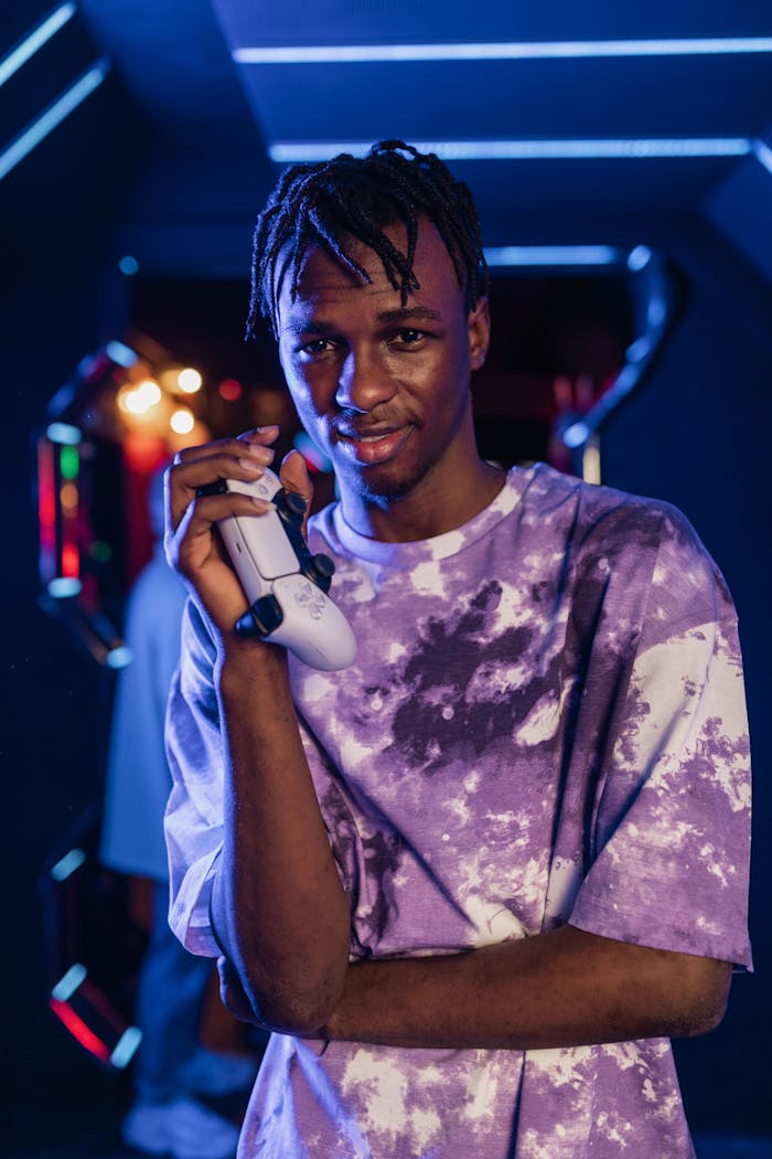 Home Portrait of a young man holding a video game controller in a neon-lit gaming room.