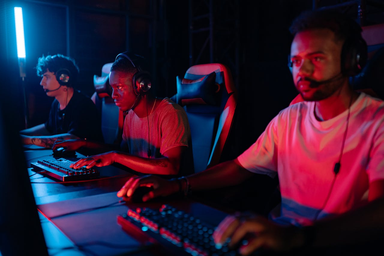 Home Three gamers immersed in a competitive setting with neon lighting, using keyboards and wearing headsets.