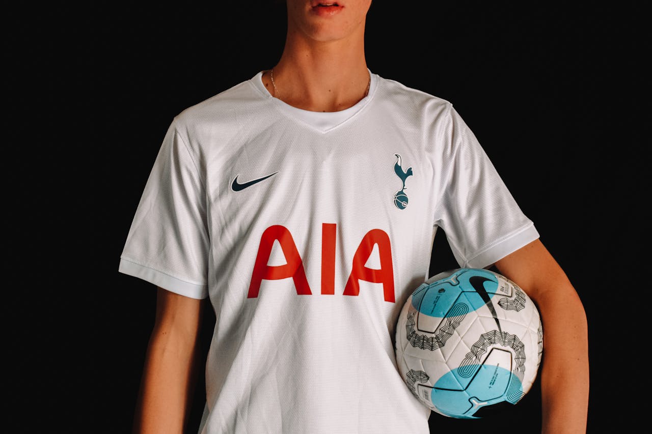 Services Adult soccer player in Tottenham Hotspur jersey holding a ball against a dark background.